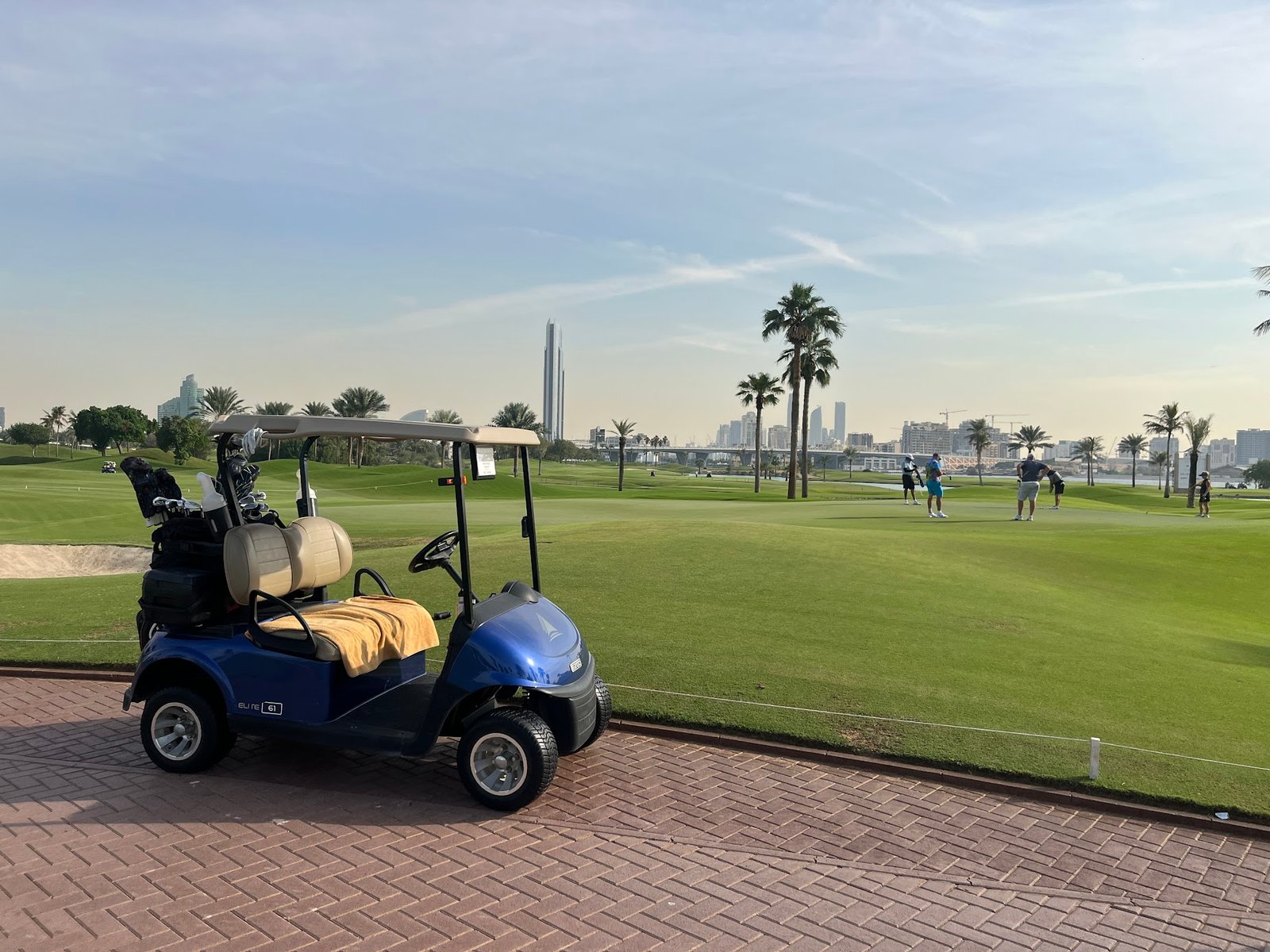 View of Dubai Creek Golf & Yacht Club featuring a lush green course, iconic sail-shaped clubhouse, and yachts docked along the creek under a clear sky.