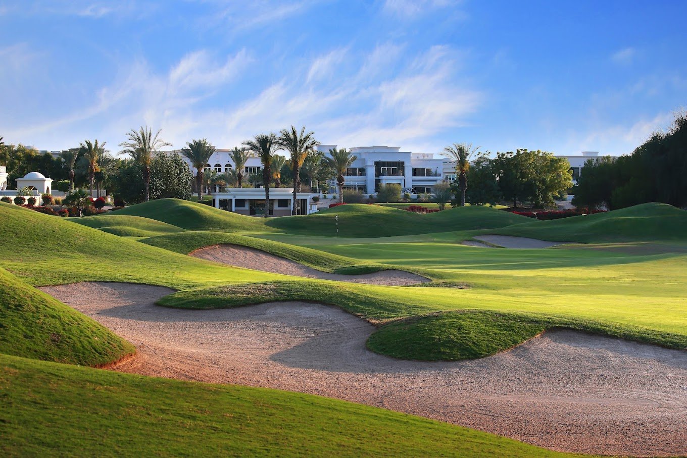 Expansive view of The Address Montgomerie Golf Club with pristine fairways, water features, and the modern hotel in the background, set against a clear sky.