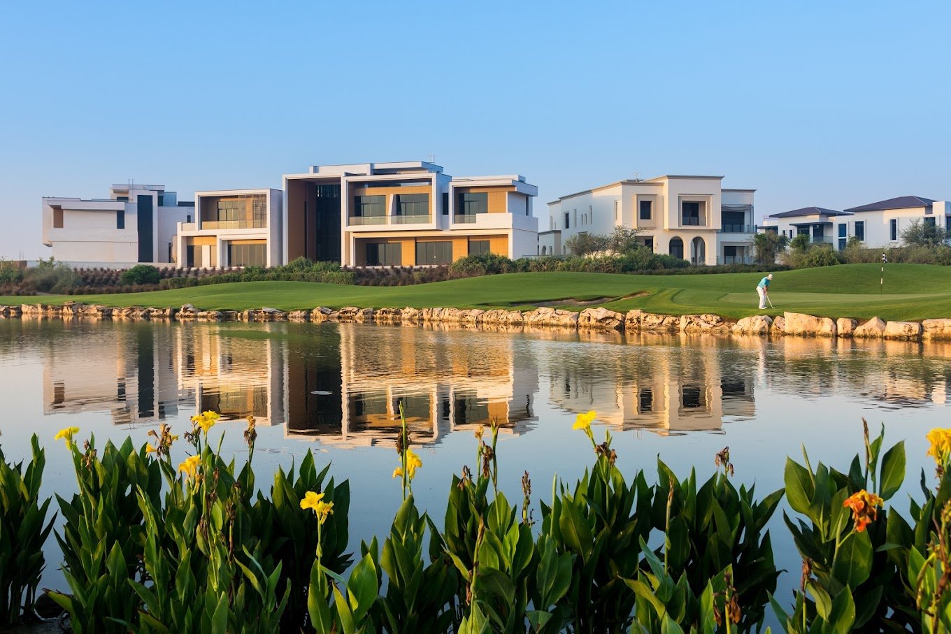 Picturesque view of Dubai Hills Golf Club with rolling green fairways, strategically placed bunkers, and the Dubai skyline in the distance under a clear sky.